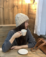 Cable Knit Beanie in beige, holding a coffee cup