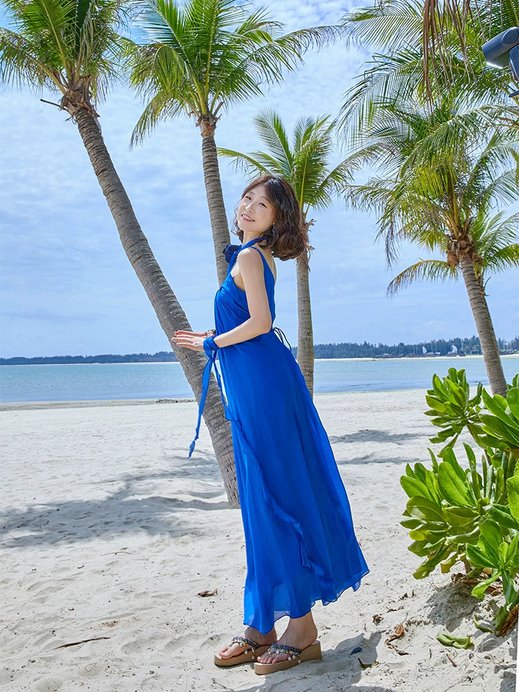 Woman smiling under palm trees in a blue strap maxi dress with a ribbon tied at her wrist