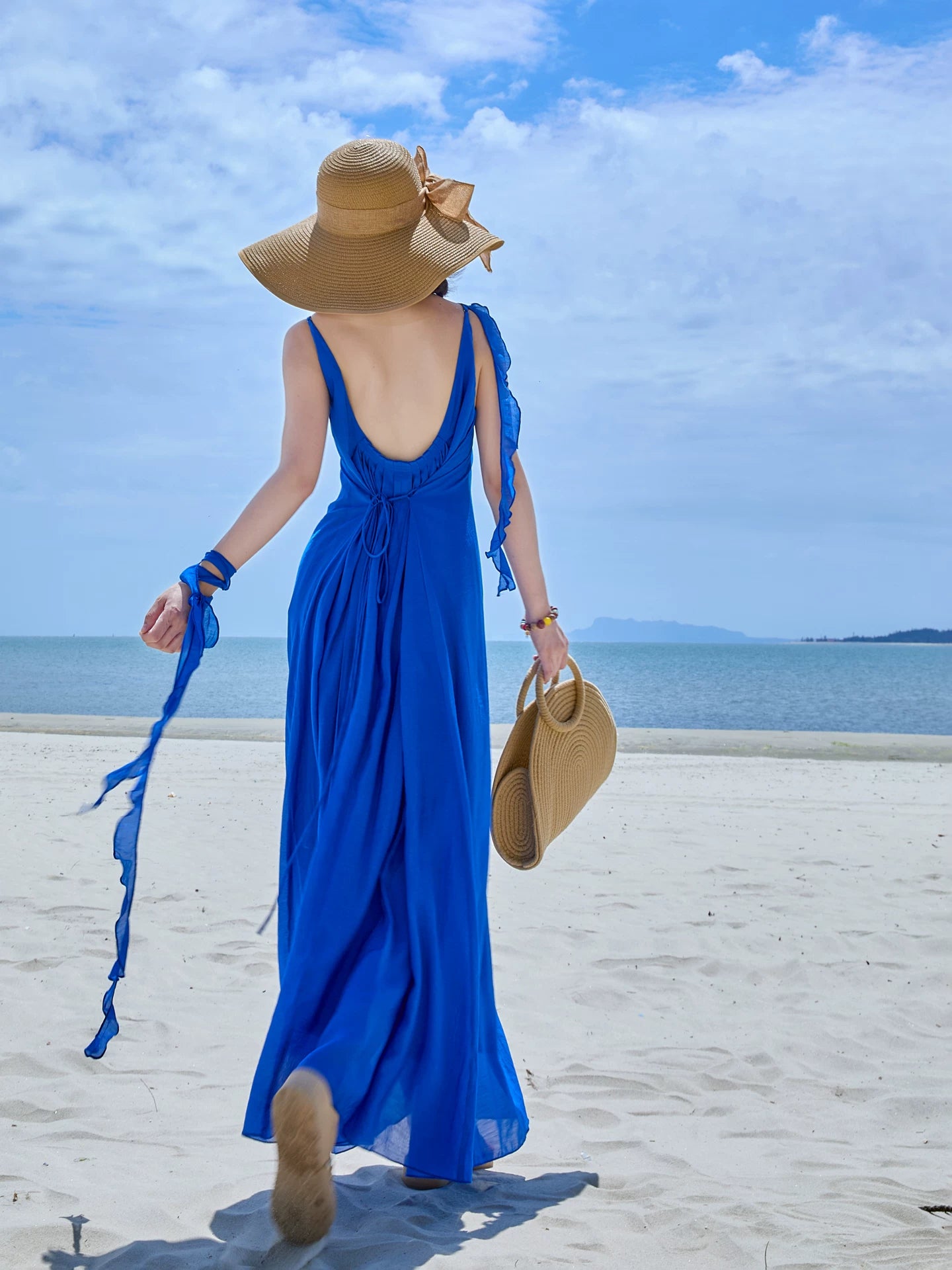 Back view of a blue maxi dress with a low open back as the woman walks toward the sea