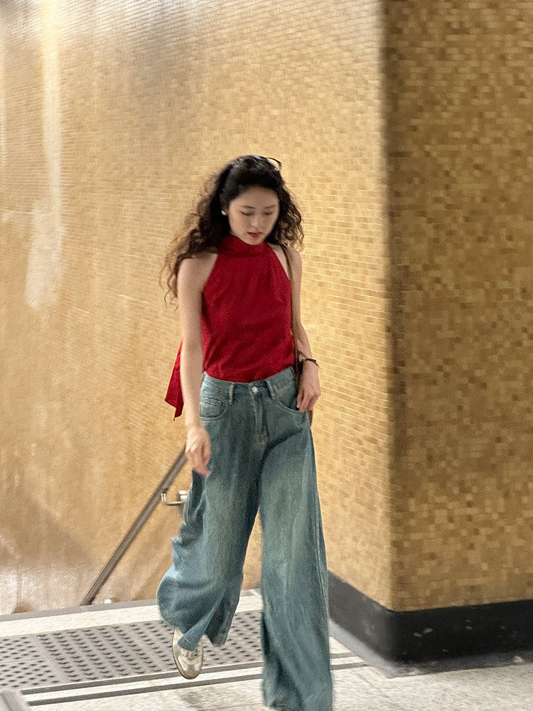 Woman on a stairway beside gold mosaic walls wearing a red high neck halter top and wide jeans