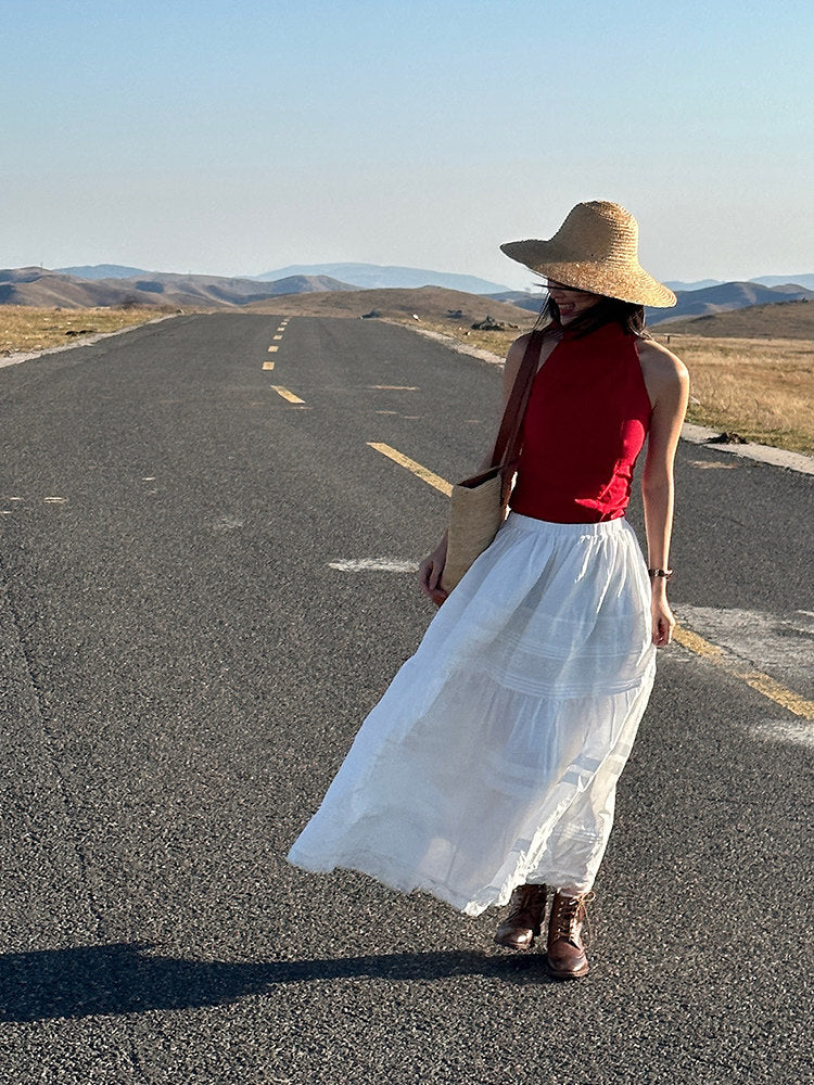 Red high neck halter top worn with a white maxi skirt and straw hat on an open road