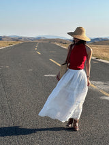 Red high neck halter top worn with a white maxi skirt and straw hat on an open road