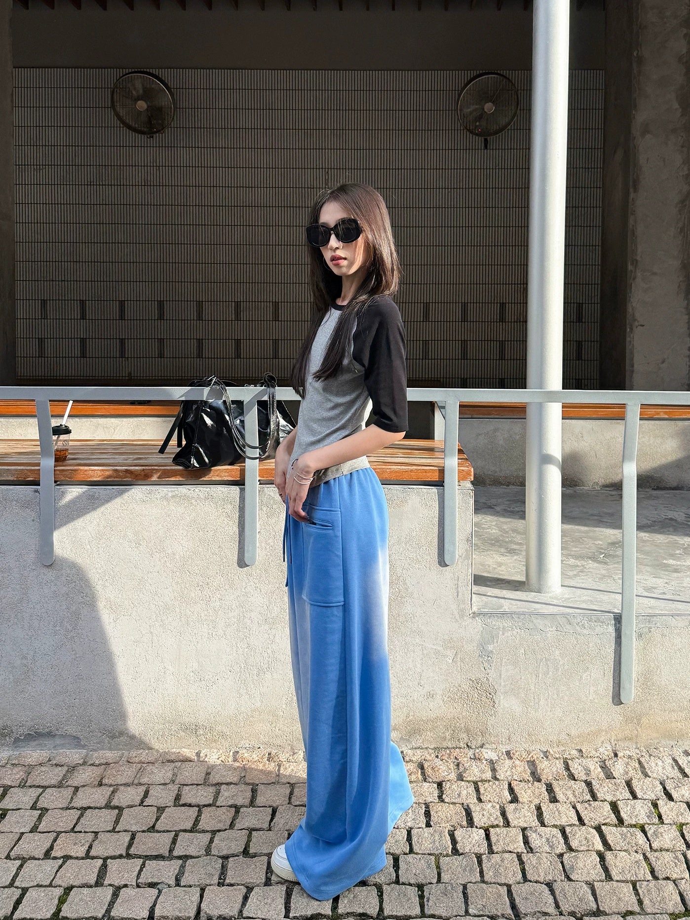 Woman in blue gradient drawstring wide pants and a raglan tee standing on a sunlit cobblestone street