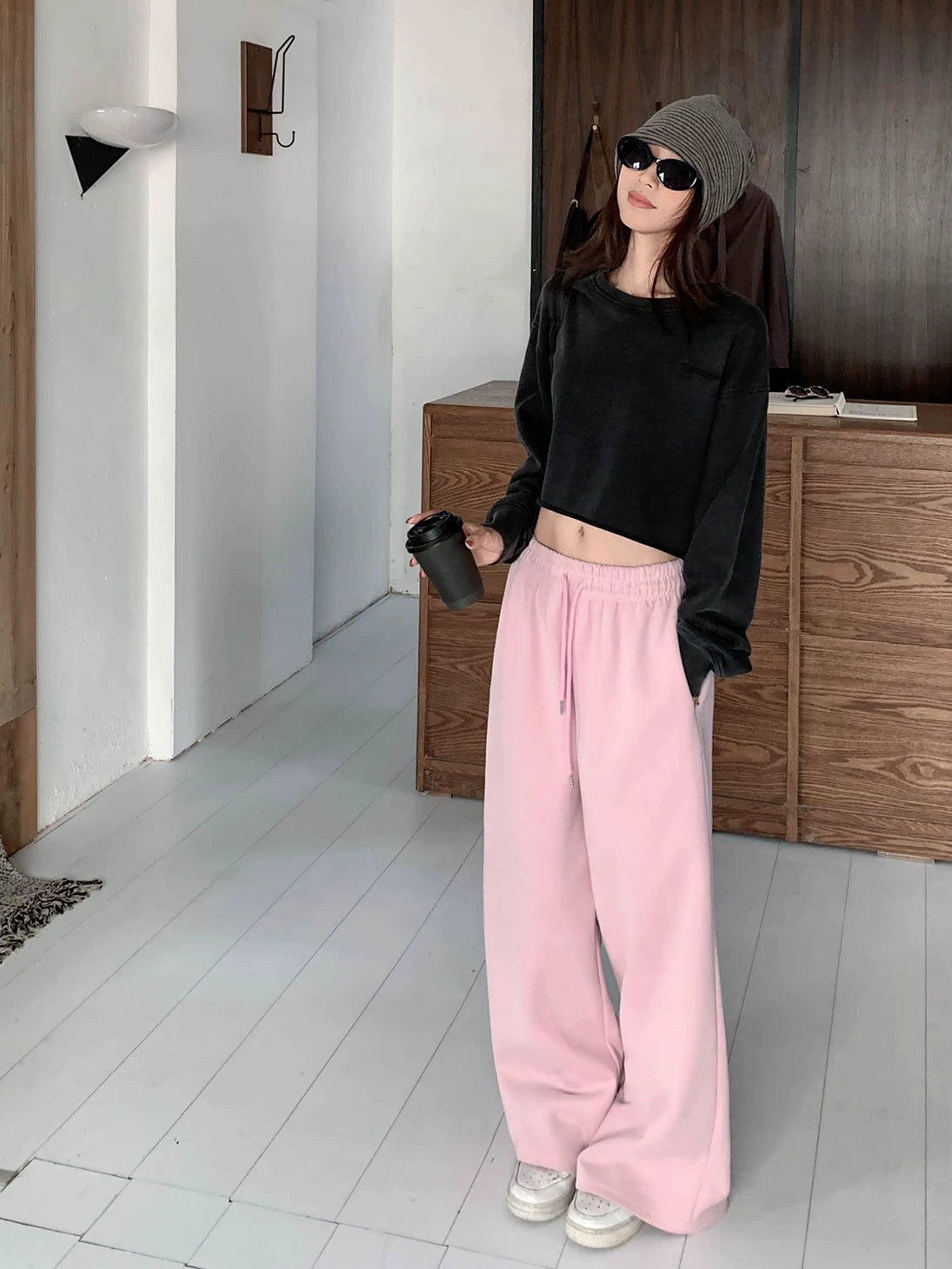Woman in pink low rise wide sweatpants and a cropped black sweatshirt, holding a takeaway cup