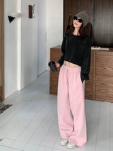 Woman in pink low rise wide sweatpants and a cropped black sweatshirt, holding a takeaway cup