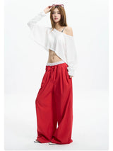 Woman in a white off shoulder crop tee and red wide pants, one hand raised to her hair