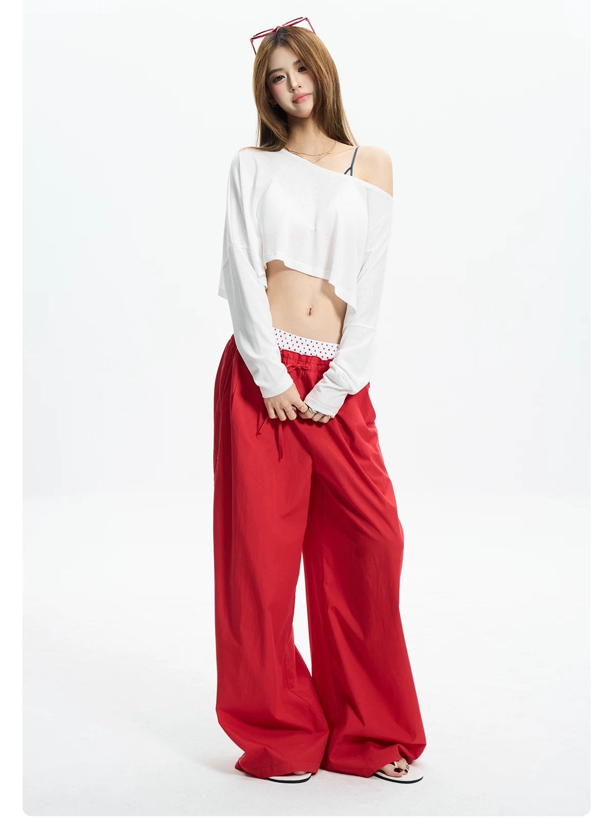 Woman standing in a white off shoulder crop tee with red wide pants