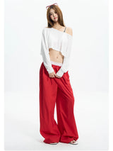 Woman standing in a white off shoulder crop tee with red wide pants